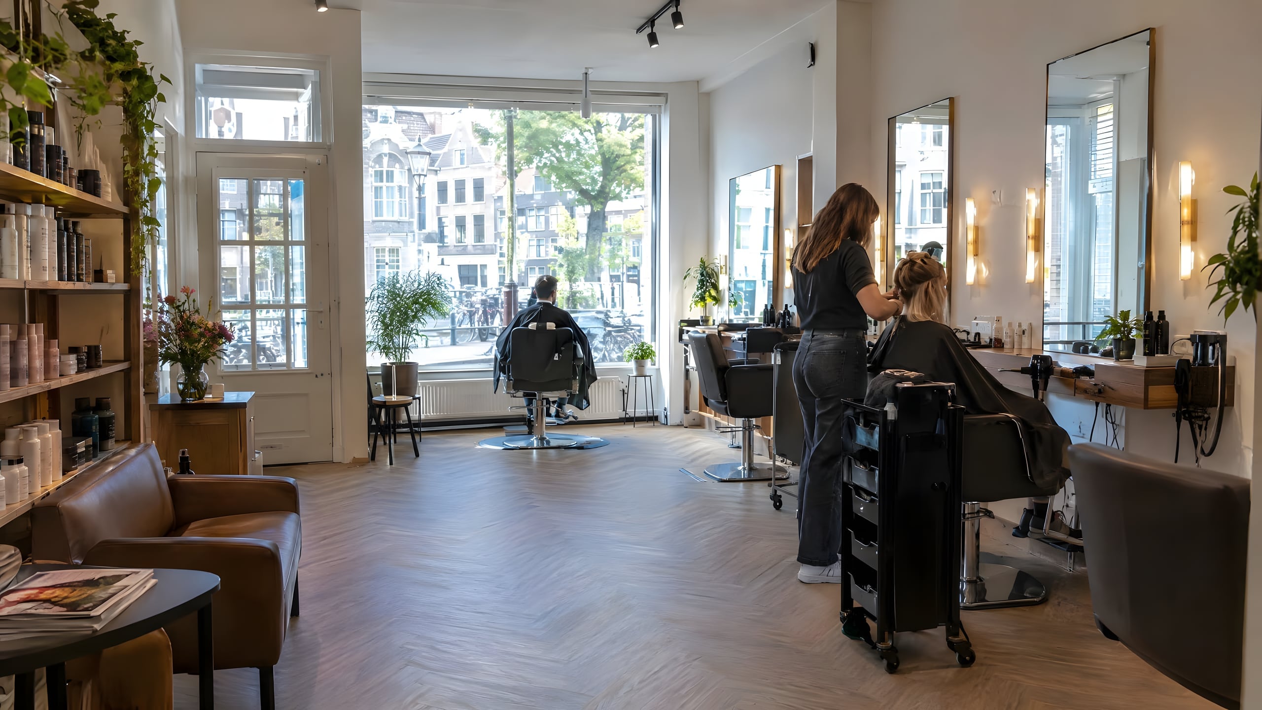 Een lichte kapsalon met kappersstoelen, spiegels en planten bij een groot raam